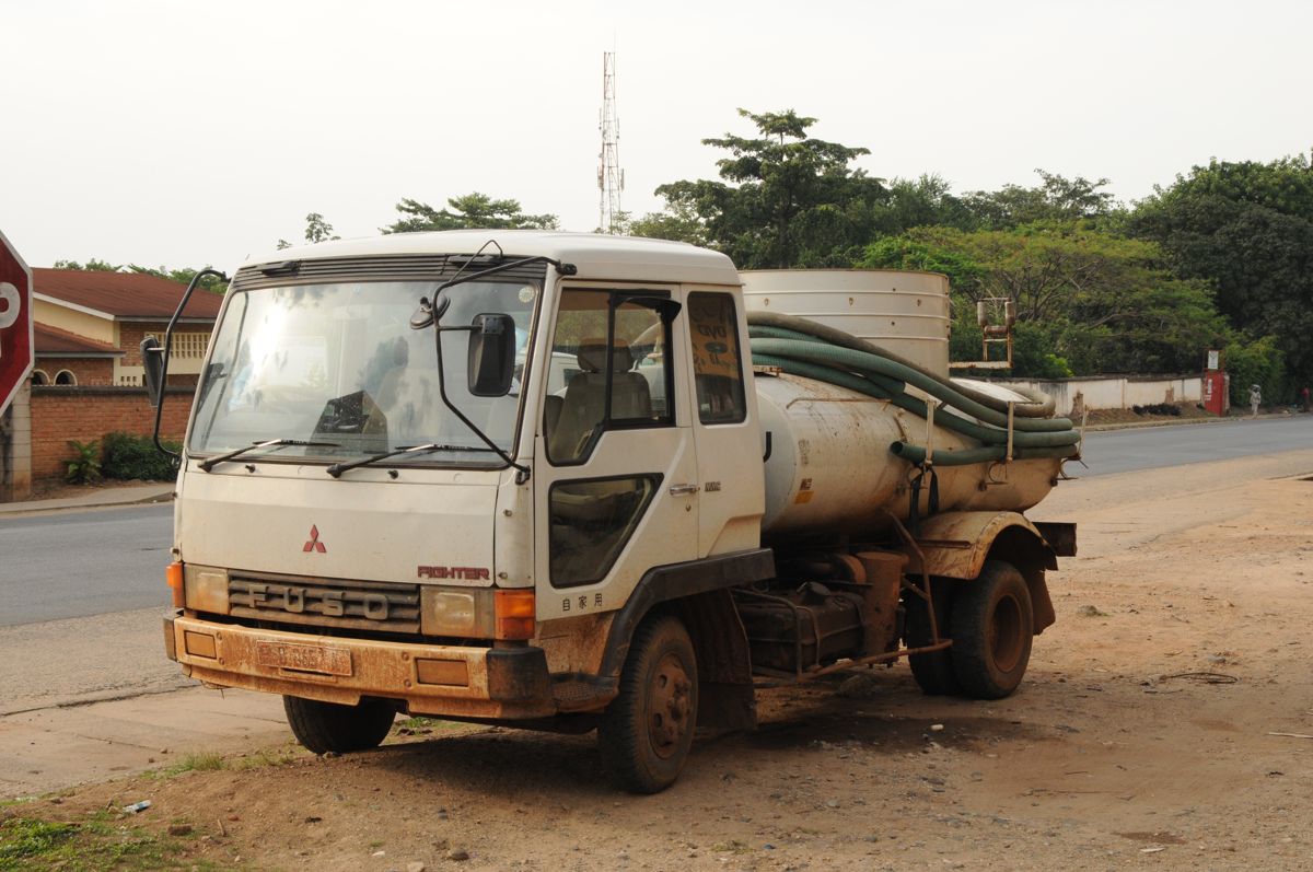 Truk vakum putih dengan tangki dan selang besar terparkir di tepi jalan, siap melakukan penyedotan septic tank