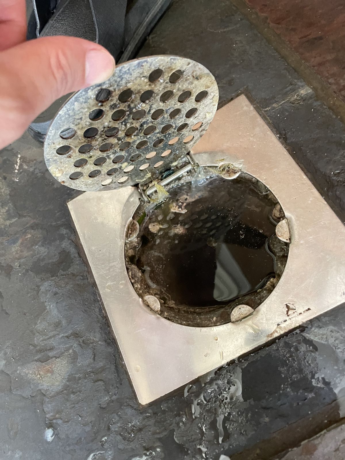 Saringan floor drain kamar mandi dibuka dan terlihat kotoran menumpuk di lubang saluran yang membuat air lambat turun